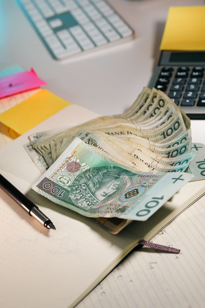 who-we-are A stack of Polish Zloty banknotes on an office table with a calculator and notebook.