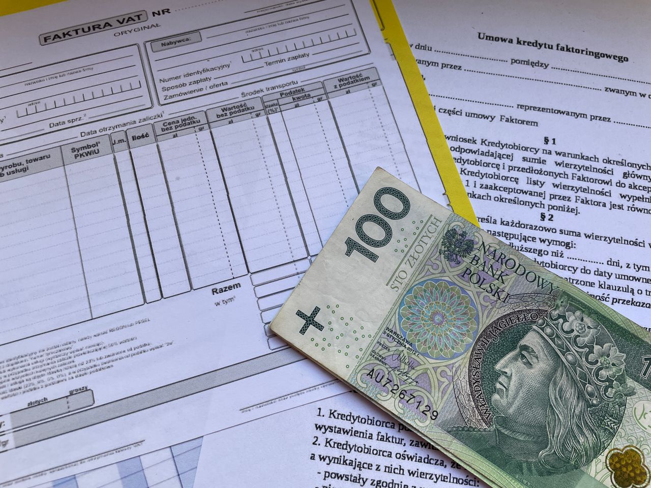 100 Polish zloty bill on top of financial documents and invoices on desk.